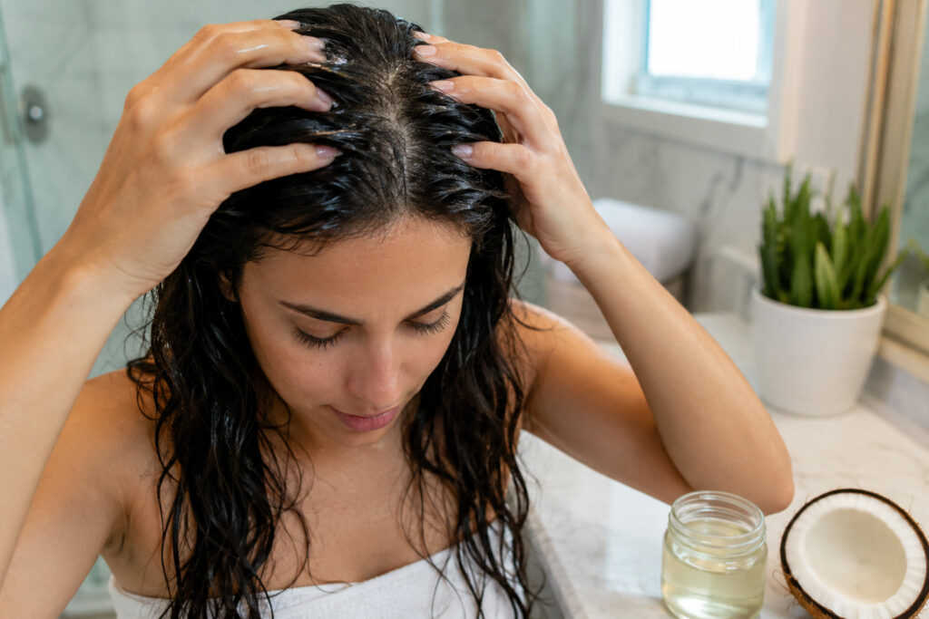 Woman applying coconut oil to scalp as a home remedy for dandruff and hair loss