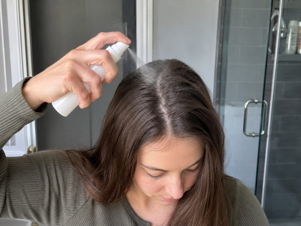 Woman spraying dry shampoo on roots to manage oily hair