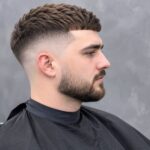 Young man with a clean skin fade haircut and textured top, viewed in side profile inside a barbershop.